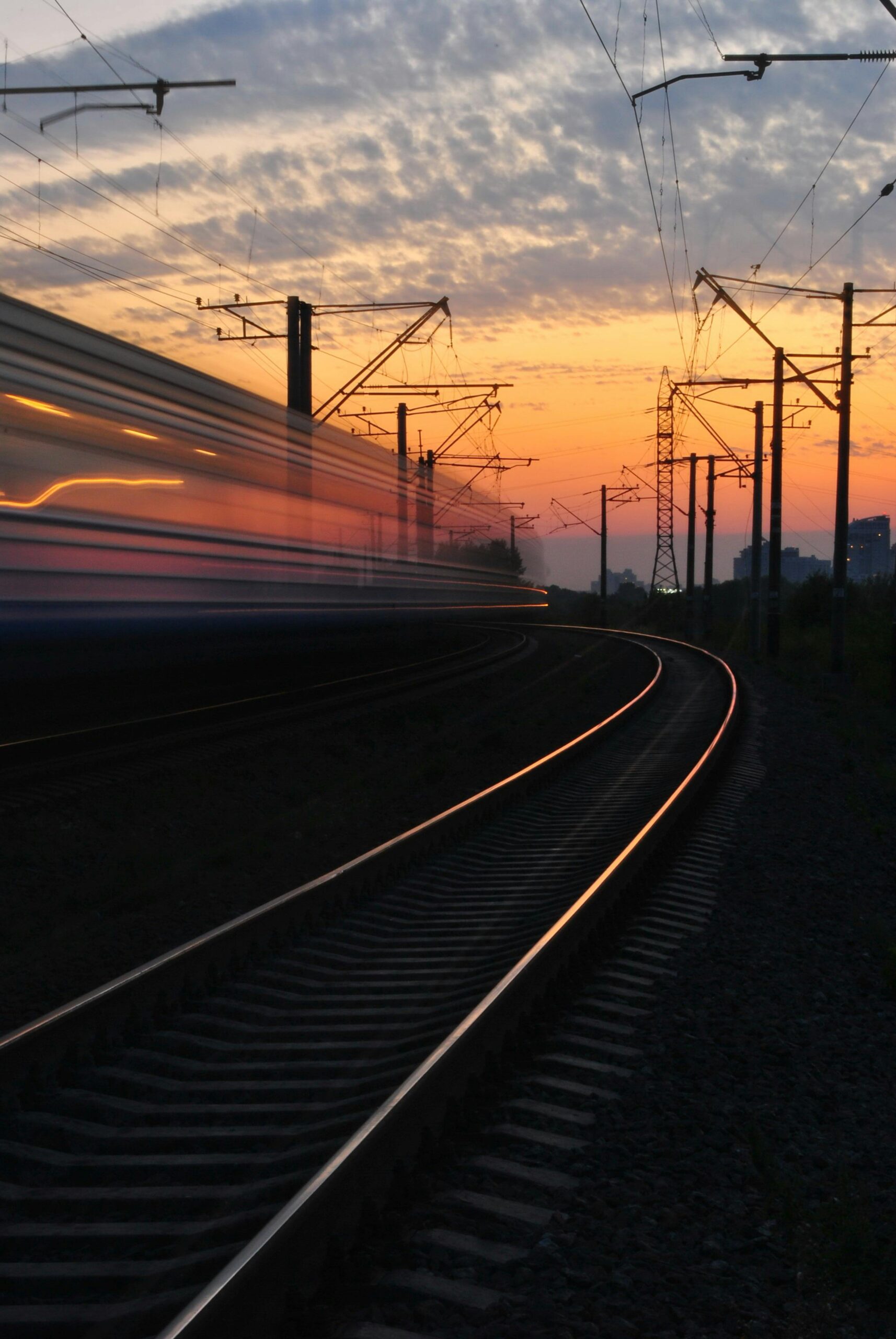 A dynamic shot capturing a blurred train speeding on curved tracks during a vibrant sunset.